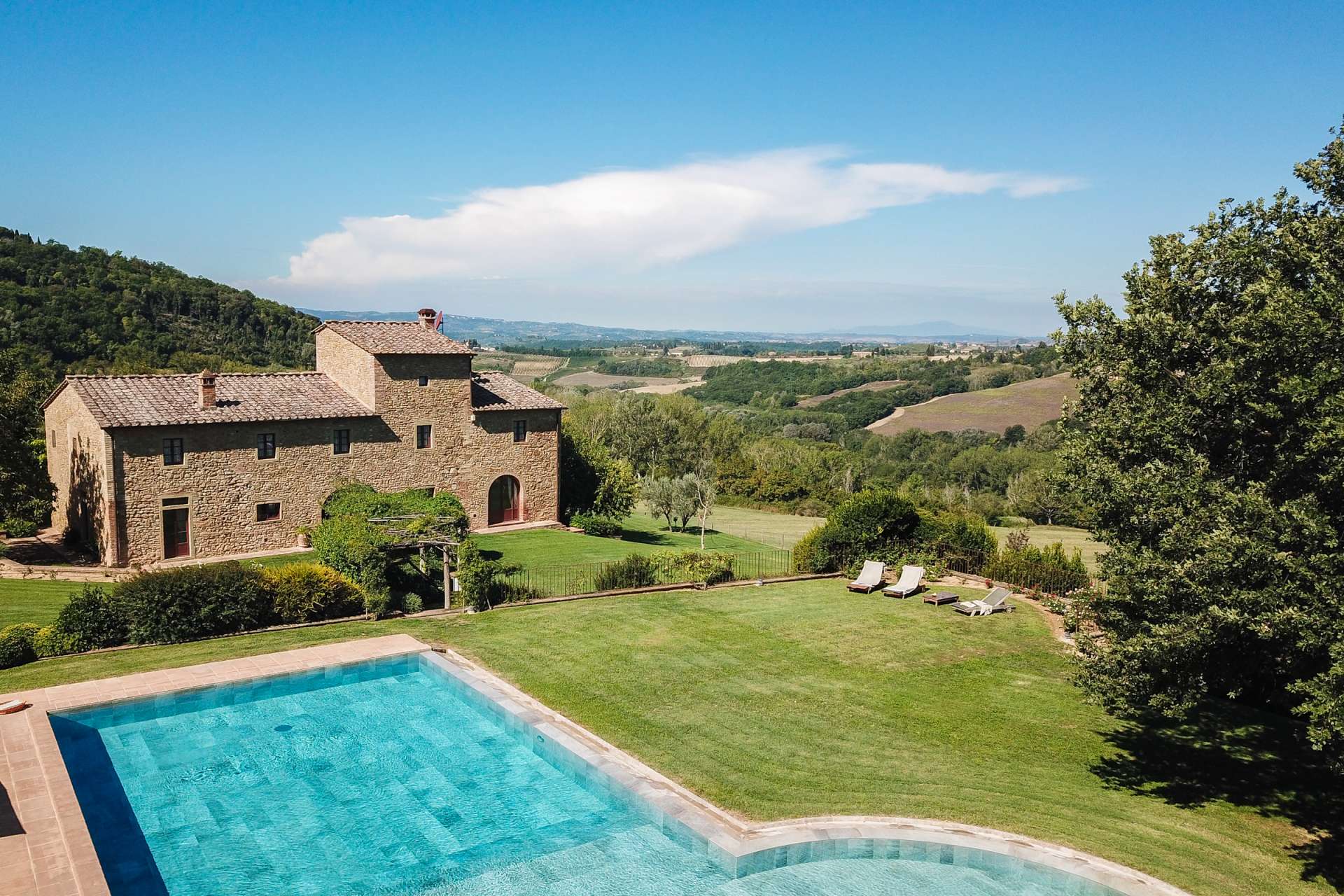 Aerial view of Podere Celli, a rustic stone villa in Tuscany with a turquoise private pool, expansive gardens, and sweeping countryside views