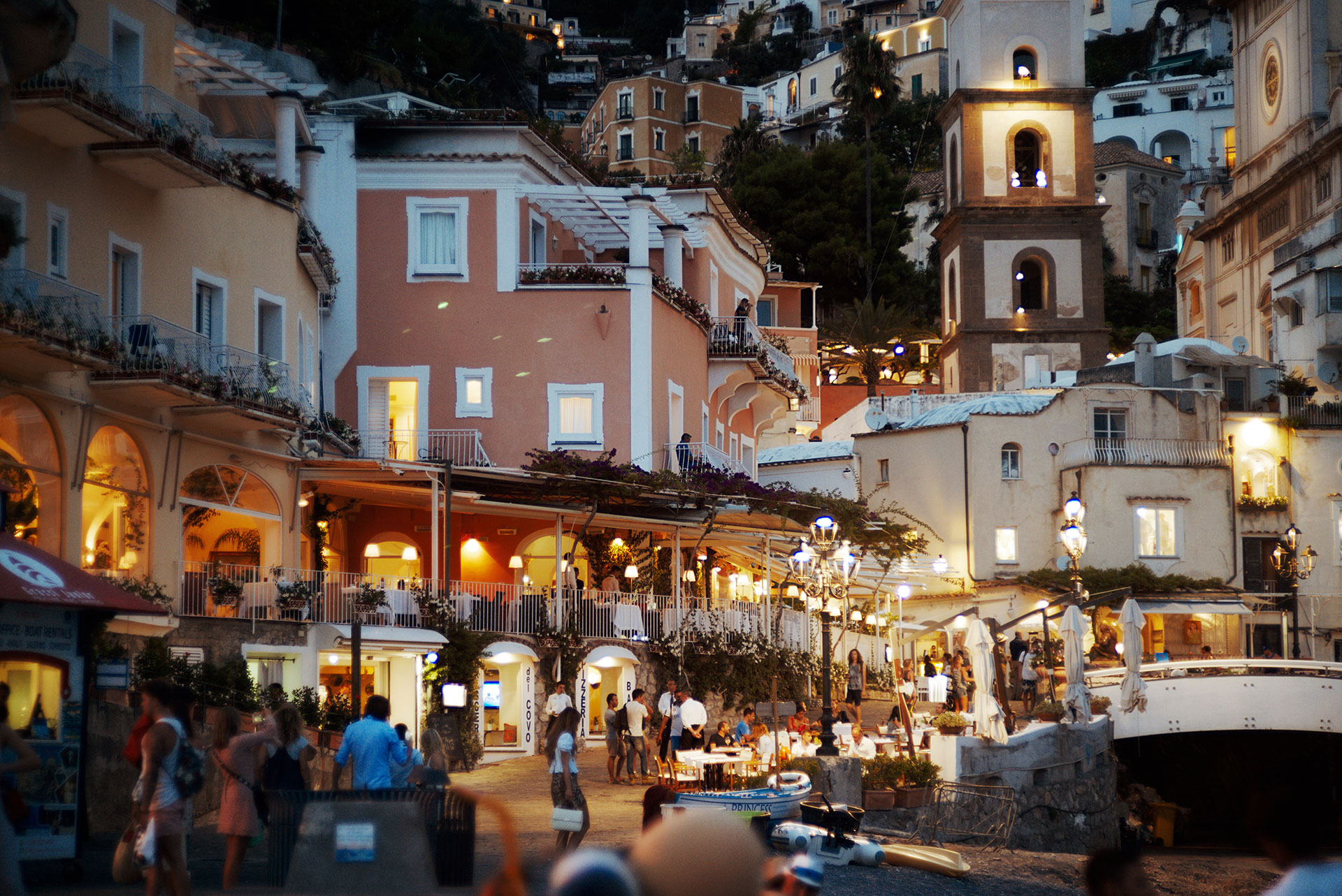 Evening view of Positano with colorful houses, restaurants and people dining under warm lights