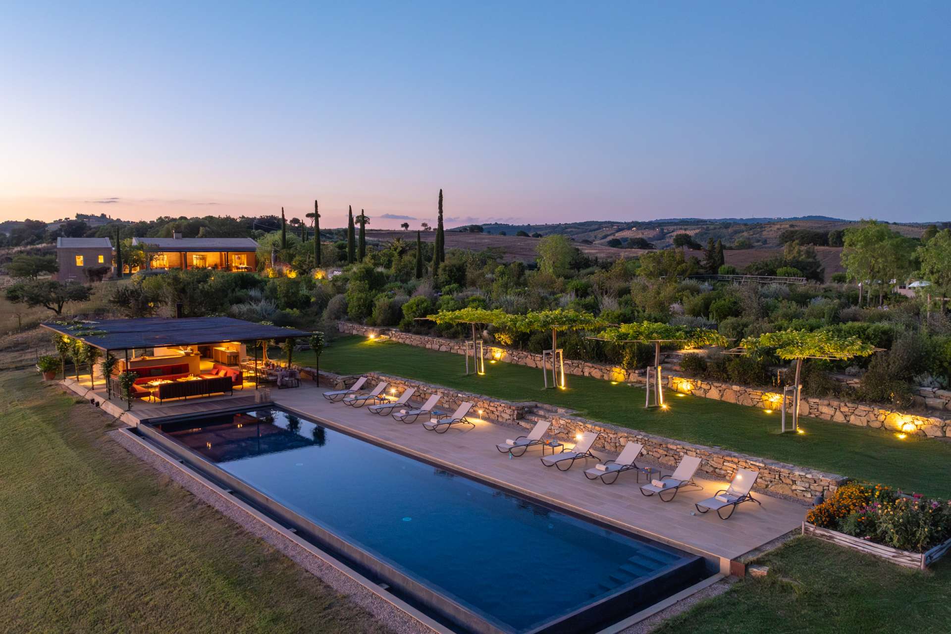 Evening view of Sartomare villa in Tuscany with illuminated garden, private pool and outdoor lounge area.