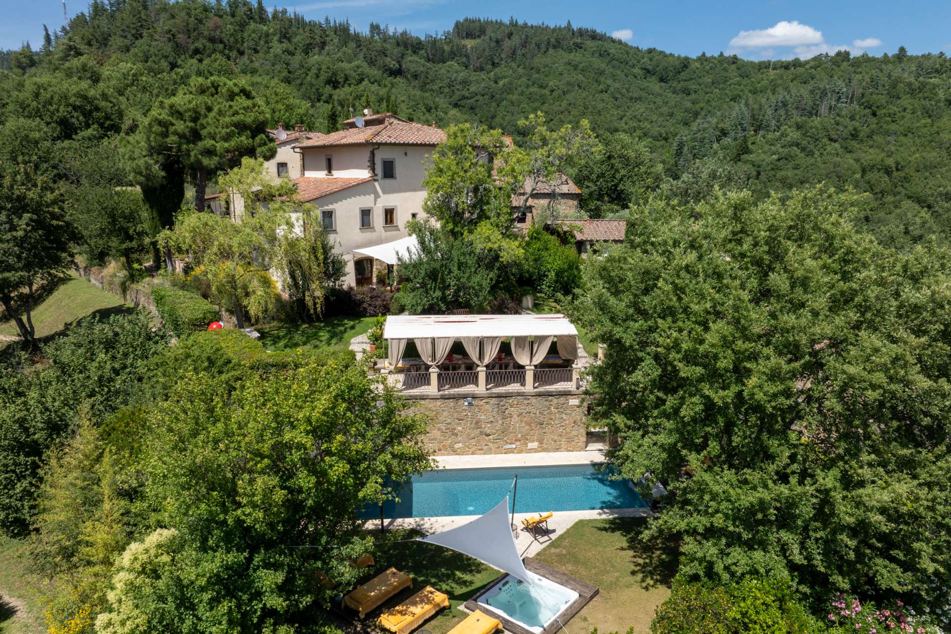 Aerial view of Villa Albizi, a 16th-century Tuscan villa in Chianti, surrounded by forested hills, with private pool, garden cabana, and outdoor jacuzzi