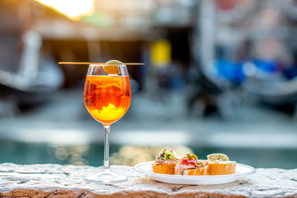 Spritz Aperol drink with venetian traditional snacks cicchetti on the water chanal background in Venice. Traditioanal italian aperitif. Image with small depth of field