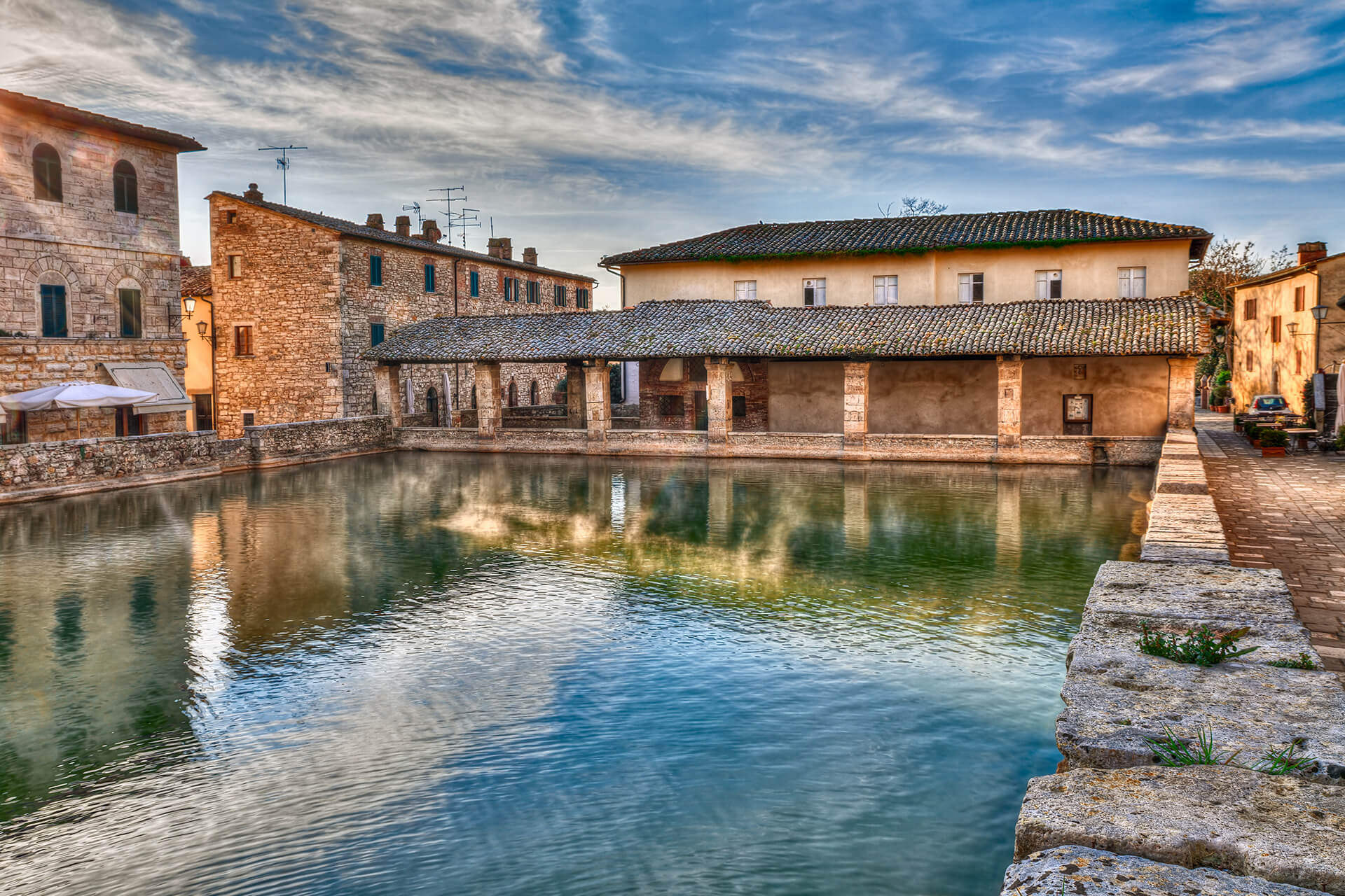 Bagno Vignoni thermal pool in Tuscany with historic stone buildings reflected in the water