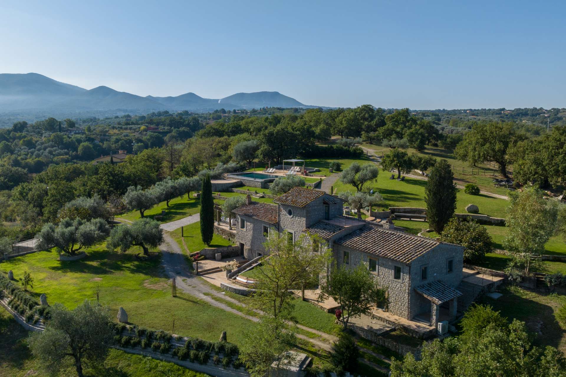 Aerial view of Villa Elaios in southern Tuscany, surrounded by olive trees and rolling hills, featuring a private pool and traditional stone architecture