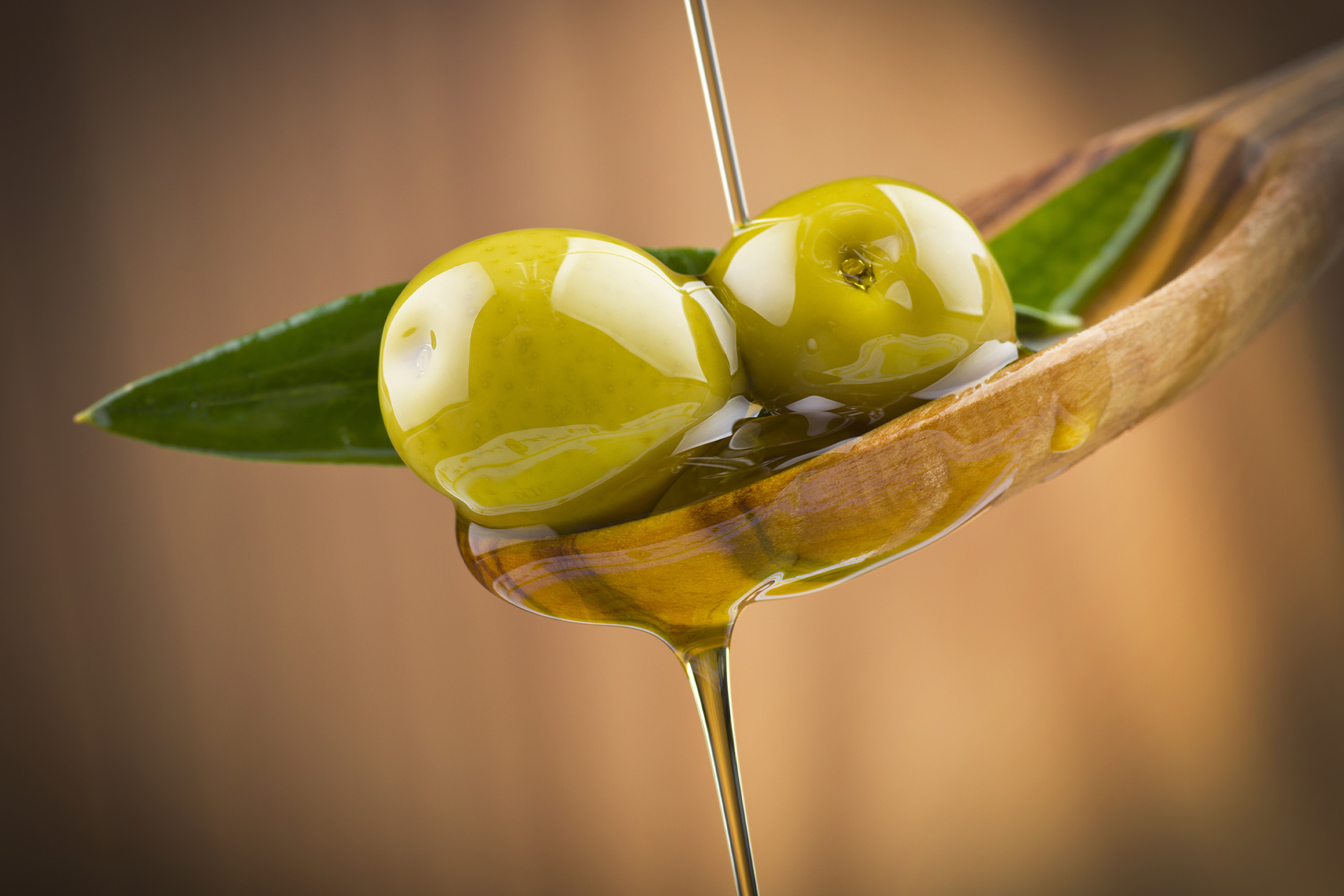 Close-up of green olives and olive oil dripping from a wooden spoon, symbolizing Mediterranean flavor