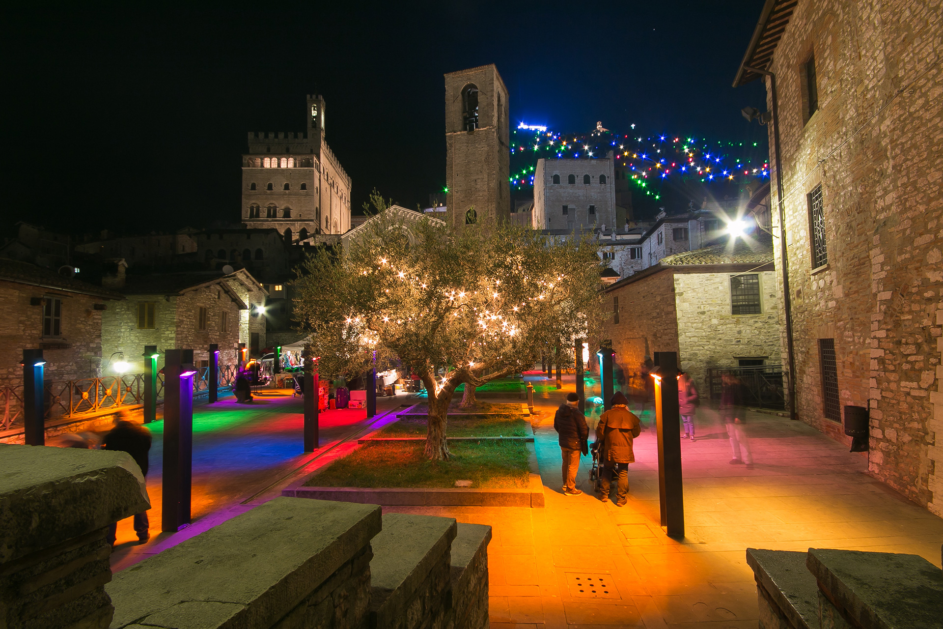 Magical Christmas atmosphere in Piazza San Giovanni in Gubbio, with illuminated decorations, colorful lights, medieval buildings, and the traditional Christmas markets at night.
