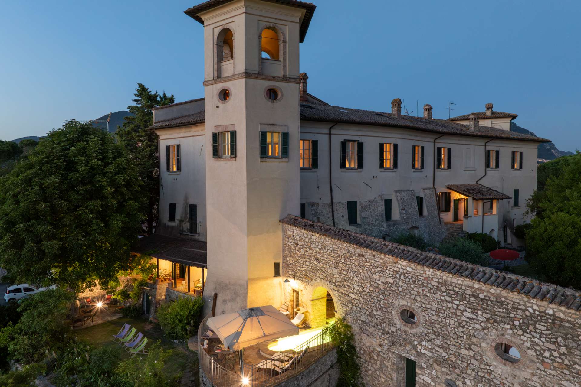 Luxury historic villa Santi Terzi at dusk in Tuscany Luxury historic villa Santi Terzi in Tuscany at dusk with illuminated windows, stone walls, and panoramic countryside setting