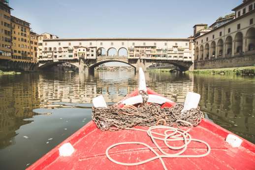 Arno Gondola Ride - A red gondola floats away from the Ponte Vecchio bridge on the river Arno.