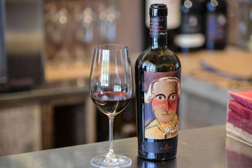 Chianti Wine Tour - A glass of red wine sits next to an open wine bottle bearing a painting of a man’s face.