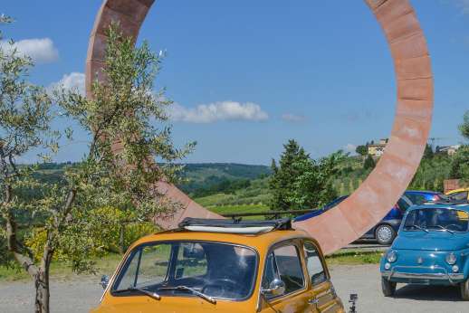 Fiat 500 Tour - Two classic Fiat 500s parked next to a large, wheel-shaped sculpture overlooking the Chianti countryside.