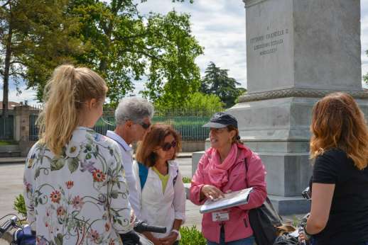 Lucca By Bike Or Foot - A tour guide points to a book next to a monument for the group.