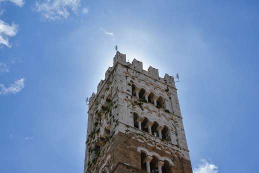 Lucca By Bike Or Foot - The top of an historic Italian tower eclipses the sun against a blue sky.