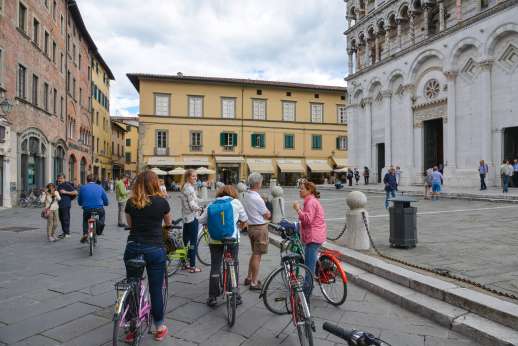 Lucca By Bike Or Foot - A group of tourists on bicycles stop to admire an historic building in Lucca.