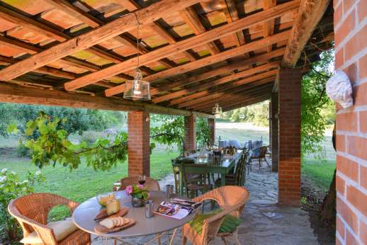 La Pergola di Montegiove - Garden loggia with a long dining table and a sitting area.