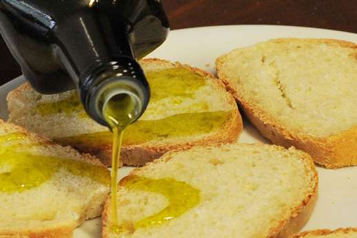 Extra virgin olive oil being poured over toasted bread in a traditional Italian food experience